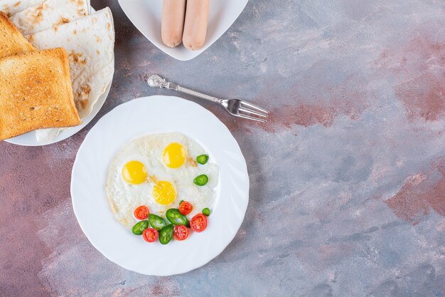 Plaat van gebakken ei met worst en brood op marmeren oppervlak.