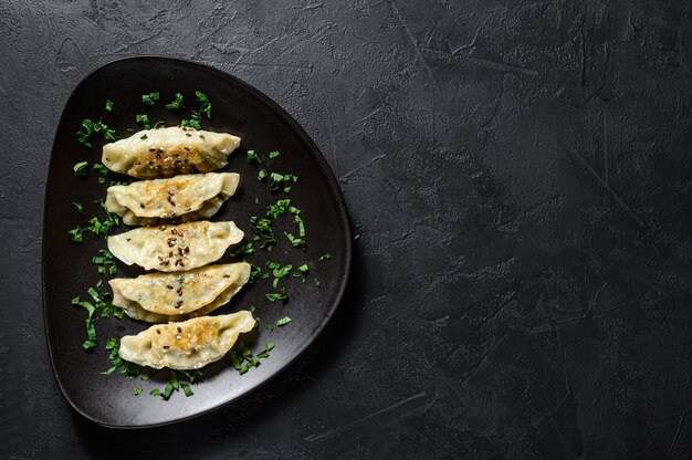 Plaat van gebakken Koreaanse dumplings op rustieke zwarte tafel. Bovenaanzicht. Ruimte voor tekst