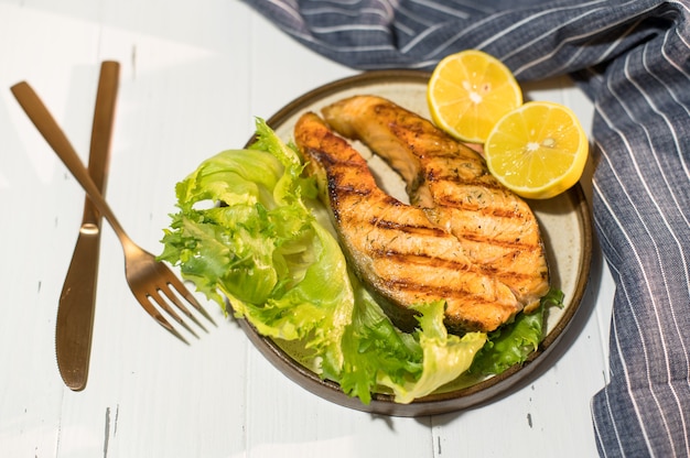 Plaat van gegrilde zalm steak met salade op houten tafel met blauw servet.