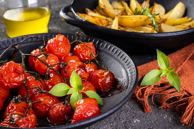 Plaat van gekonfijte tomaten en geroosterde aardappelen met rozemarijn in ijzeren braadpan op donkere achtergrond.