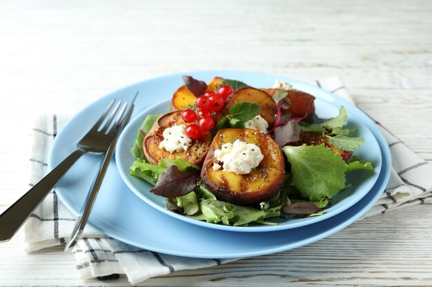 Plaat van salade met gegrilde perzik op witte houten tafel