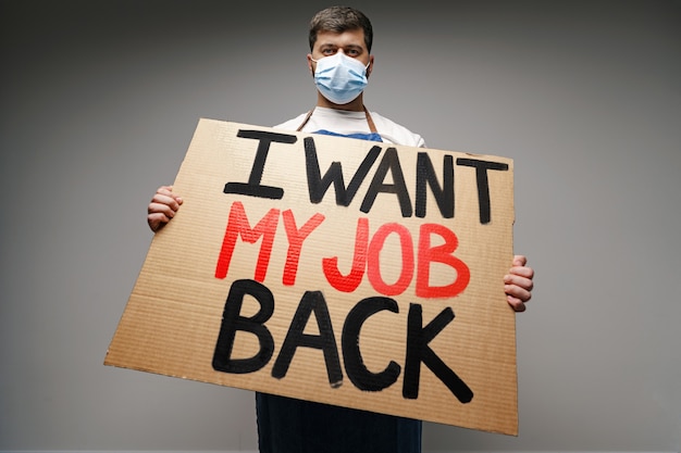 Placard 'I want my job back' in hands of protester man wearing mask.