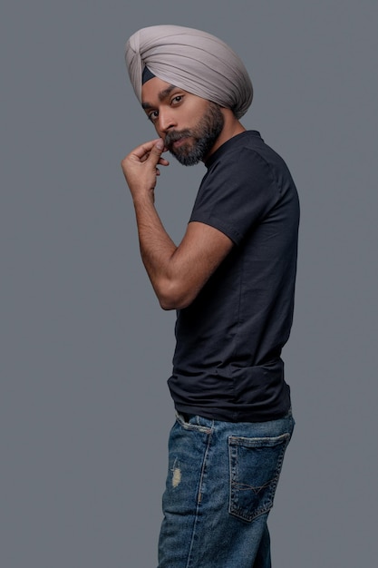 Placid attractive guy in the turban and casual clothes posing for the camera against the gray background