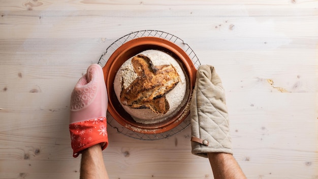 Placing hot clay pot with freshly baked sourdough bread on a cooling rake