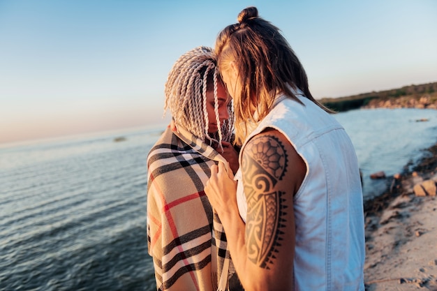 Plaid on shoulders. Loving caring man putting plaid on shoulders of his girlfriend standing near sea