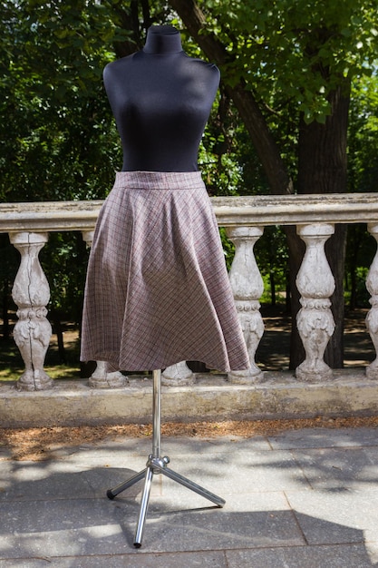 マネキンにチェック柄のスカート 緑の木々を背景にストレートにカットされたスカート 天然素材の生地を使用したオーダーメイドの女性用スカート 仕立て