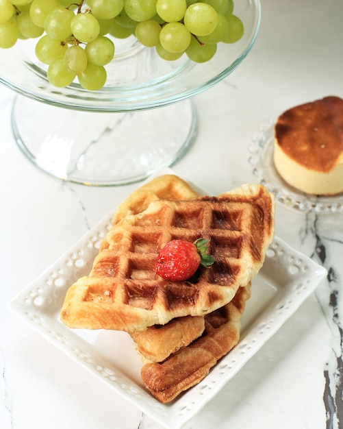 Semplice croffle croissant cialda croissant su piatto bianco, tavolo in marmo bianco con fragola sulla parte superiore e uva verde sullo sfondo. questo snack popolare in corea del sud