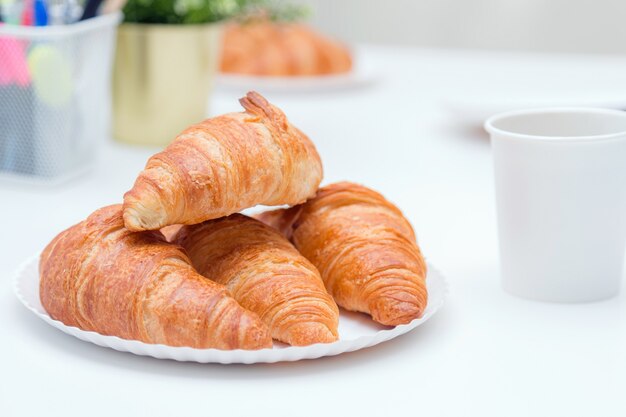 Plain croissants on top of each other on the plate on the office table.