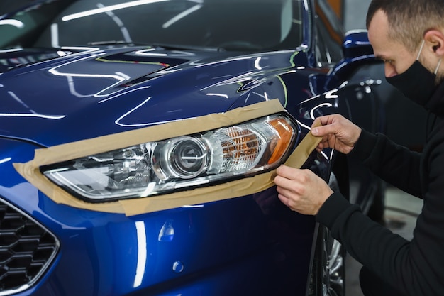 Plakband op autokoplampen. Koplamp polijsten. Detailing auto buiten.