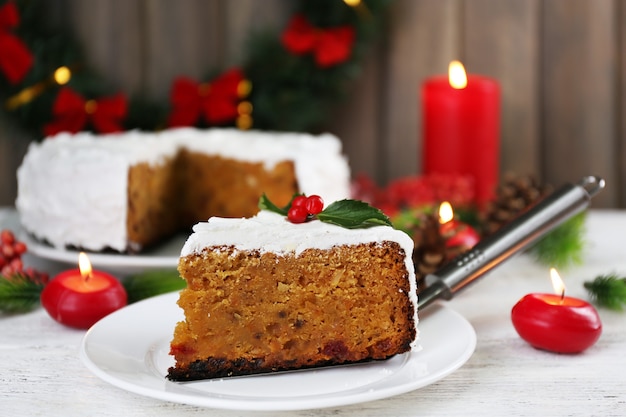 Plakje cake bedekt room met kerstversiering op tafel, op houten muur achtergrond