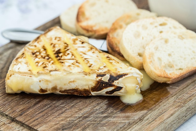 Plakje gegrilde camembert met geroosterde baguettes en cranberryjam geserveerd op een houten plank