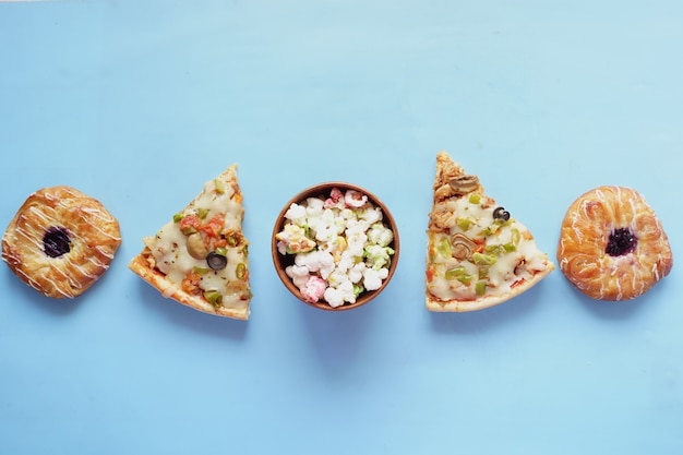 Plakje kaas pizza op een bord, donuts en popcorn op blauw.