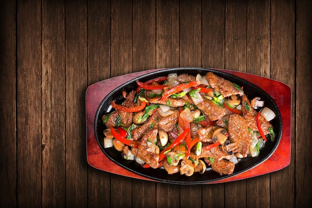 Plakjes gebakken vlees met uien, paprika, champignons, in een koekenpan, op een bord. Bekijk top.