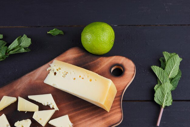 Plakjes gele harde kaas op een houten bord met citrusvruchten met verse munt op een houten zwarte achtergrond Close-up van een stilleven Bekijk van bovenaf