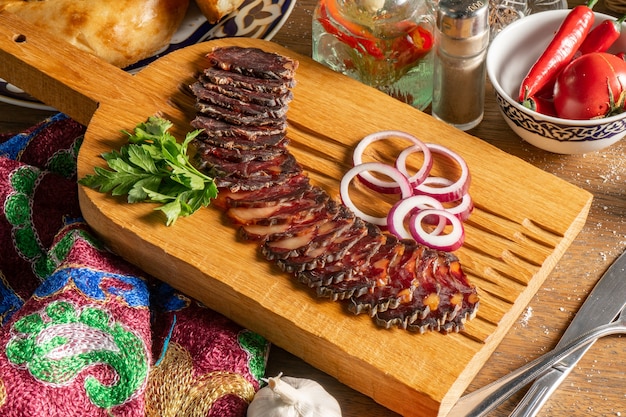 Plakjes huisgemaakte gedroogde paardenvleesworst met koriander en rode ui, in plakjes gesneden en geserveerd op een houten snijplank