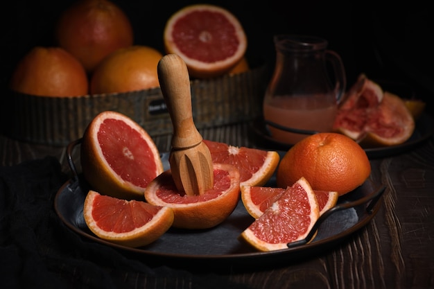 Plakjes verse grapefruit bereid voor het maken van vers geperst sap op een schotel, donkere achtergrond