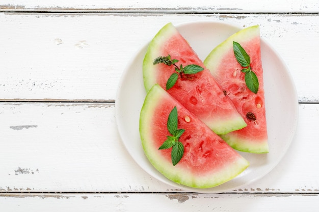 Plakjes verse verse watermeloen op een bord op een witte houten achtergrond Fruit en munt om dorst te lessen Bovenaanzicht met kopieerruimte