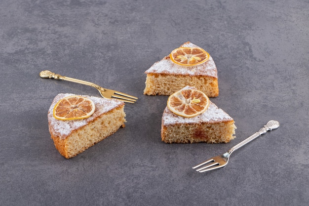 Plakjes zelfgemaakte cake met citroenen op stenen tafel.