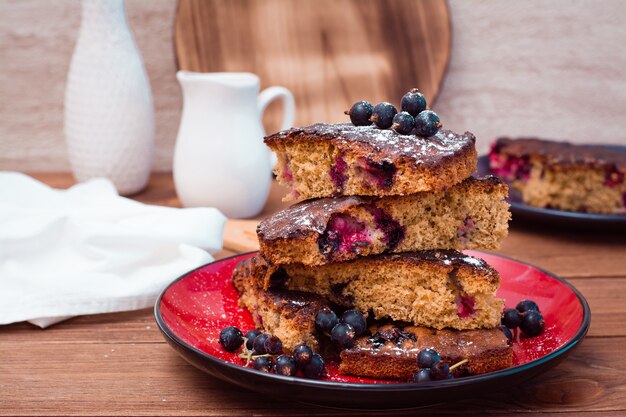 Plakken van zoete cake met zwarte bes op een plaat op een houten lijst