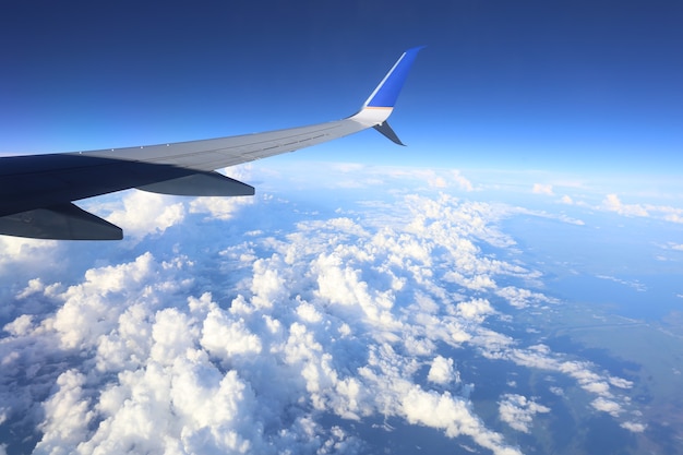 A planes wing in the sky with beautiful blue clouds on the side of the window