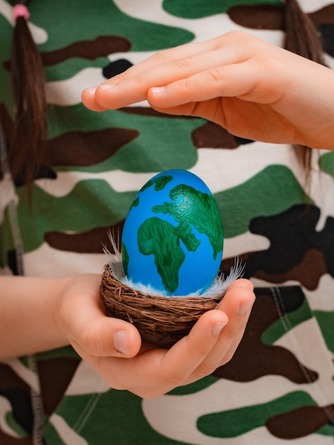 Photo planet earth in the shape of an egg in childrens hands closeup the concept of global problems of humanity peace to the world no war