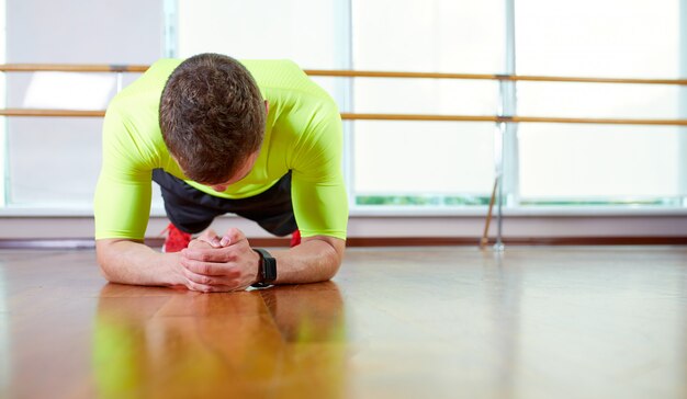 Plank it Уверенный мускулистый молодой человек, носящий спортивную одежду и делающий положение доски, тренируясь на полу в интерьере лофта