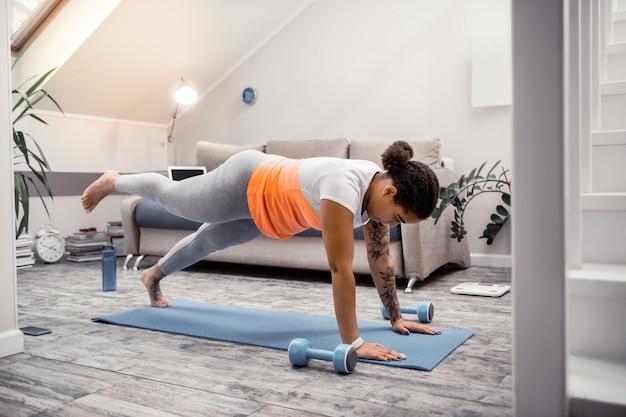 Plank on yoga mat. Strong African American woman standing in plank while having special equipment around