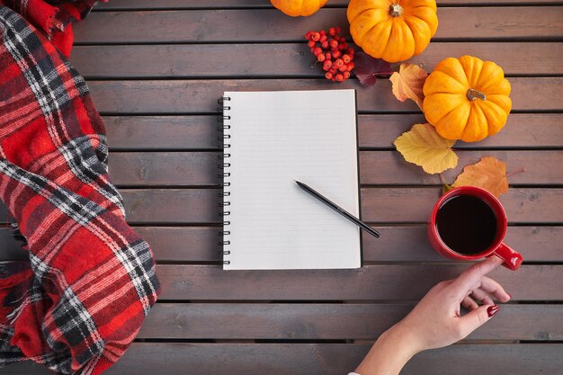 Plannen om lijst te doen. Samenstelling van de herfststemming op een houten tafel. Het jonge Europese meisje met rode manicure op spijkers houdt in handen rode kop