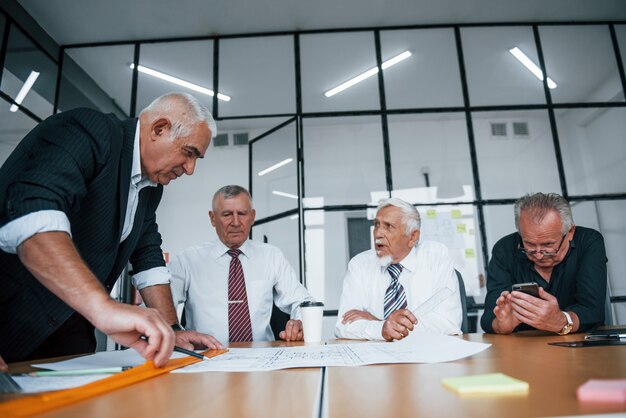 Planning construction by measuring it on paper. Aged team of elderly businessman architects have a meeting in the office.