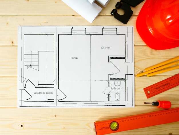 家の建設の計画。修理作業。木製の背景に建物、ドライバー、ヘルメット、その他のツールの図面。