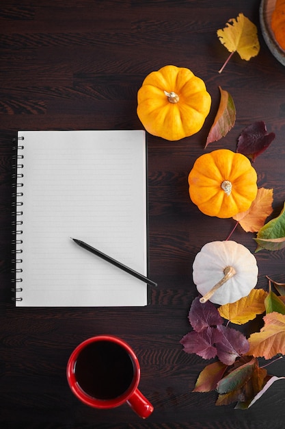 Planning om lijst te doen. Samenstelling van de herfststemming op een houten tafel met pompoenen, lijsterbes en bladeren. Open Kladblok en zwarte koffie in de rode kop en op grijze houten tafel, drankje opwarmen