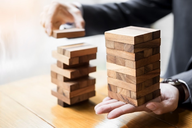 Planning, risk and wealth strategy in business concept, businessman and insurance gambling placing wooden block on a tower.