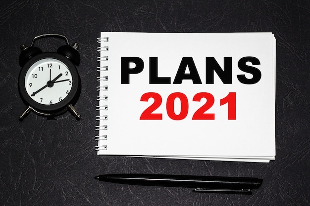 PLANS 2021 inscription on a white fragment. notebooks, watch and a pen on the table for information