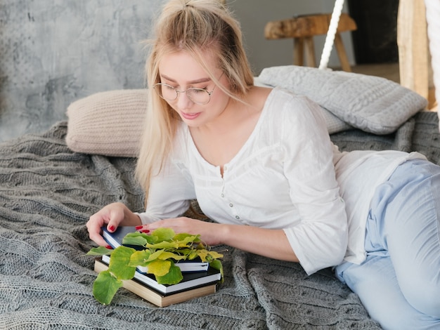植物生物学者の余暇。自宅の居心地の良いベッドで本を読んでいる眼鏡の女性科学者の肖像画。