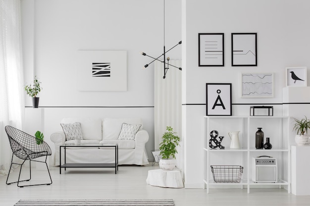 포스터와 램프가 있는 흑백 아파트 내부의 소파와 안락의자 근처에 식물