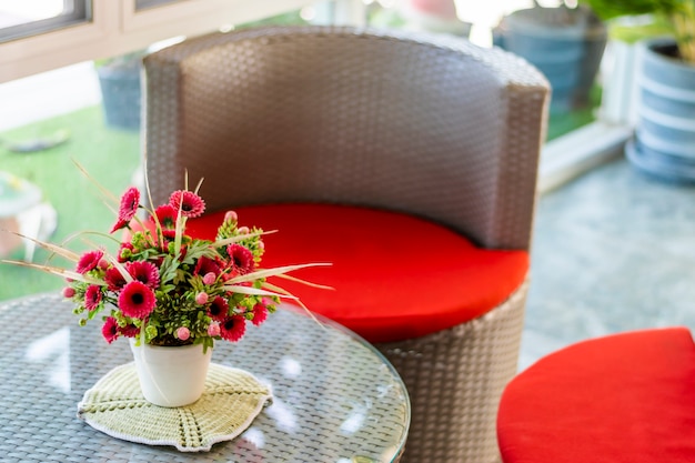 Plant pot with fake leaves and flowers, set on a glass table.