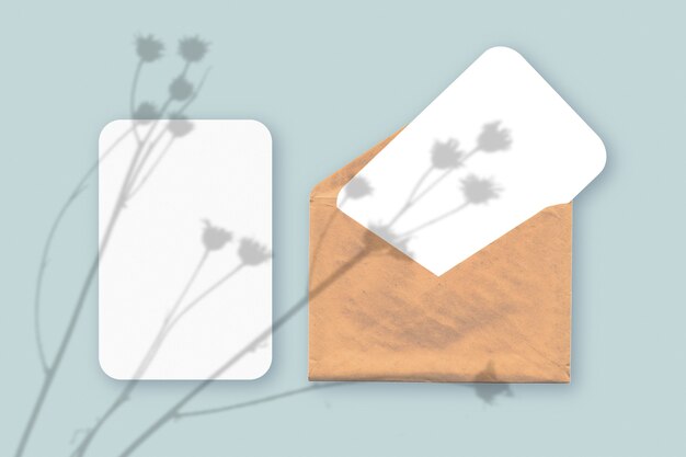 plant schaduwen op envelop met twee vellen gestructureerd wit papier op een blauwe tafelachtergrond table
