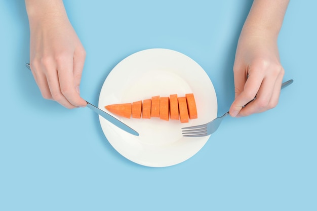 Plantaardig dieet en rauw voedsel Vrouwelijke handen met een vork en een tafelmes over een bord rauwe wortelen