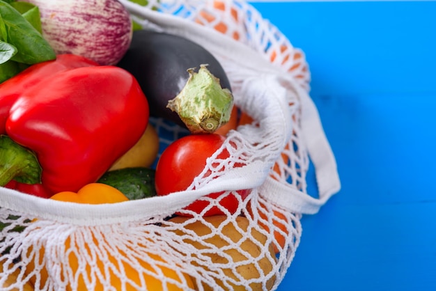 Plantaardige mand op blauwe houten achtergrond seizoensgebonden groenten peper aubergine tomaten komkommers in witte mesh string bag