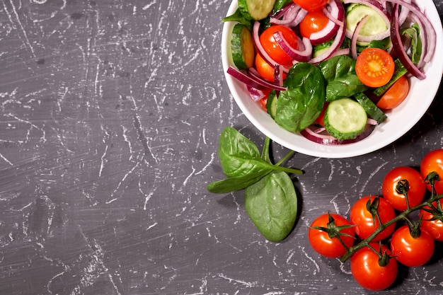 Plantaardige salade in een witte plaat op een grijze achtergrond, naast de Bulgaarse peper, tomaten