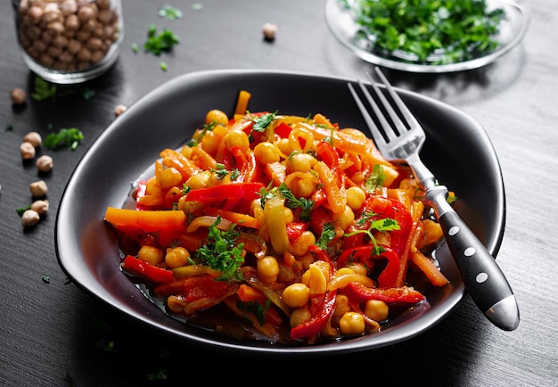 Plantaardige stoofpot van kikkererwten, wortel, paprika, ui, knoflook en tomatensaus met citroen op de donkere tafel oosterse keuken