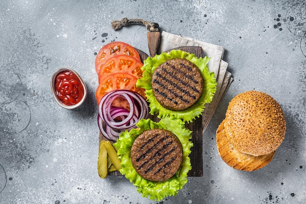 Plantaardige vleesloze burgers met vegan gegrilde pattie, tomaat en ui op een houten serveerplank. Grijze achtergrond. Bovenaanzicht.