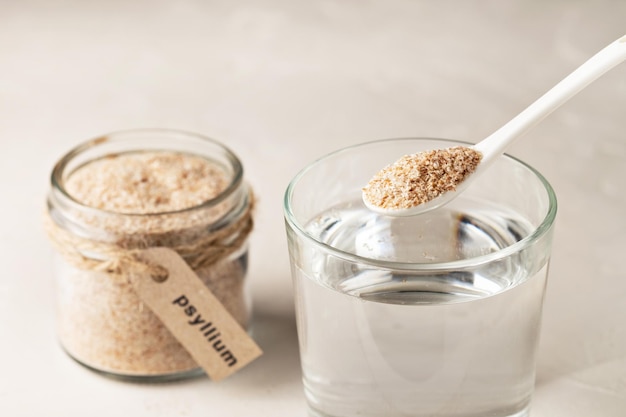 Plantain husk in a jar with the inscription psyllium and a glass of water on a light background.