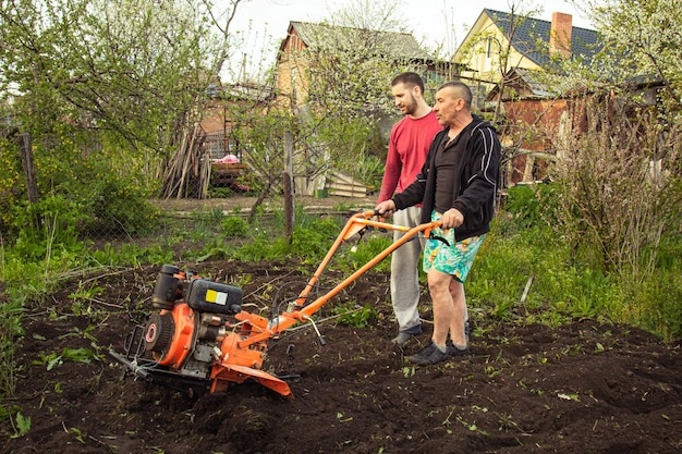 Planting vegetables under the walkbehind tractor A man with a walkbehind tractor in the garden Manual work with equipment An elderly man teaches a young boy to plow the land