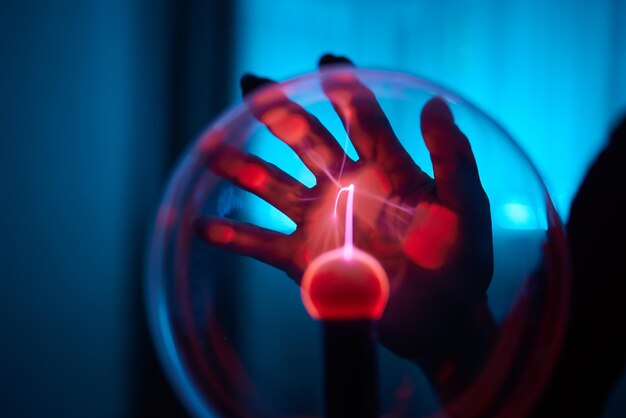 Photo plasma ball hands holding plasma light ball plasma ball light ray science finger touching plasma ball with smooth magenta blue flames electromagnetic fields in a glass globe