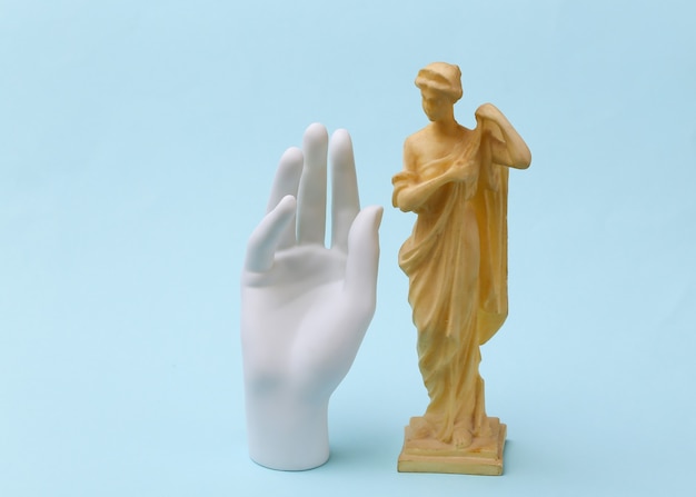 Mano in gesso e statua antica su sfondo blu.