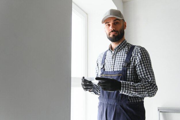 Photo plasterer in blue working uniform plastering the wall indoors