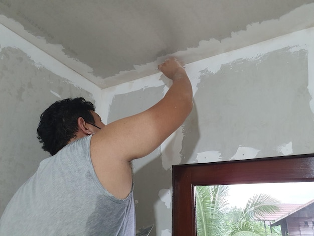 Photo plasterwork and wall painting preparation asian male applying plaster or filling drywall patch