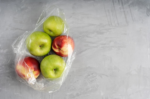 Plastic bag full of ripe apples and nectarines on concrete