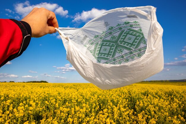 Photo a plastic bag in the hands against the background of a rapeseed field.
